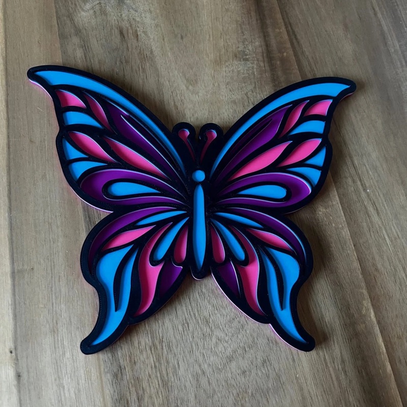A layered 3D printed butterfly in blue, pink and purple with black outlines