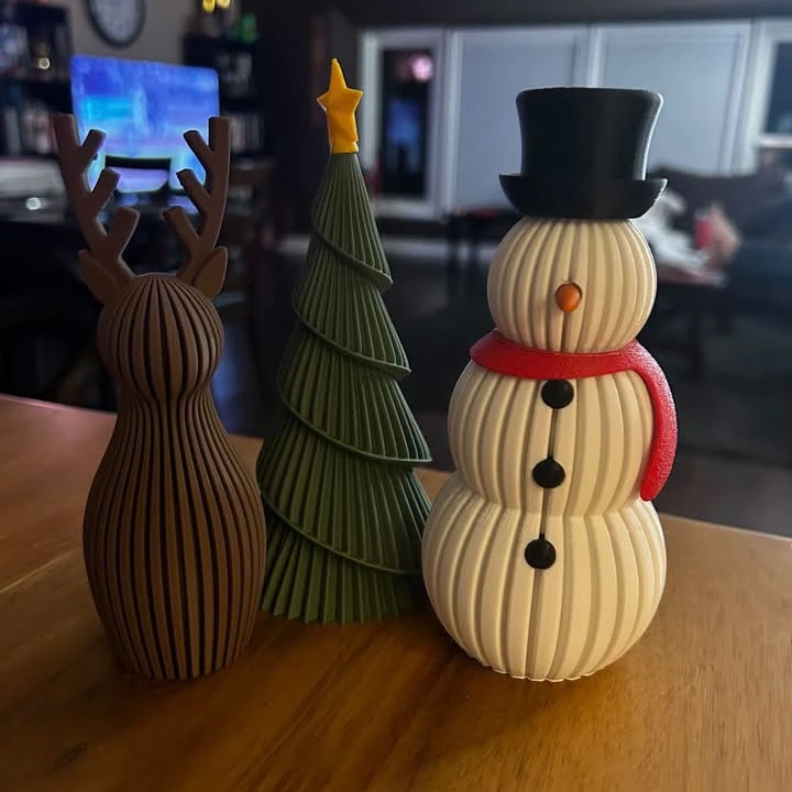 3D printed holiday decorations: a ribbed reindeer, a spiral Christmas tree with a star and a snowman in a top hat and red scarf